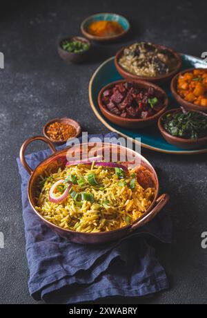 Un assortiment de plats indiens pakistanais végétariens vibrants et savoureux, y compris le riz biryani, servis dans de petits bols en bois sur un plateau rustique Banque D'Images