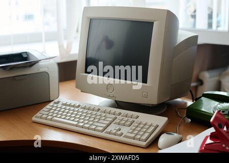 Configuration d'ordinateur vintage comprenant moniteur CRT, clavier et imprimante sur le bureau en bois, créant un environnement de travail nostalgique Banque D'Images