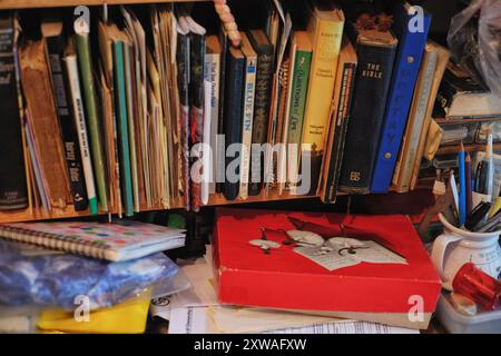 Une vieille boîte de chocolat rouge avec des ballerines, des épines de livre délavées, des papiers, des cahiers et des crayons dans une tasse, des parents vieillissants vivant à la maison dans l'encombrement du baby-boomer Banque D'Images
