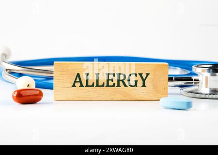 Texte d'allergie écrit sur un bloc de bois avec un stéthoscope couché à côté, des pilules, des vitamines sur un fond blanc Banque D'Images