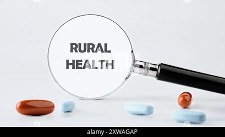 Concept médical. MOTS DE SANTÉ RURALE écrits à travers une loupe sur un fond gris dans une composition avec des comprimés et des vitamines. Photo conceptuelle Banque D'Images