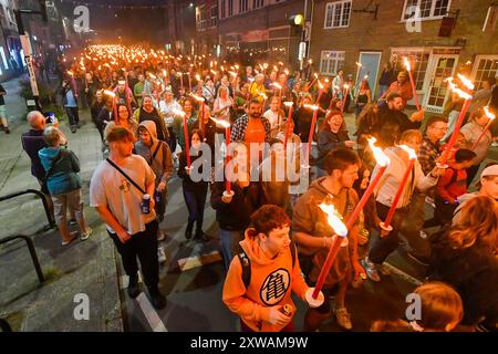 Bridport, Dorset, Royaume-Uni. 18 août 2024. Des centaines de personnes portant des torches flamboyantes participent à la procession annuelle des torches du carnaval de Bridport. La procession de Two Mile a commencé à l'hôtel de ville de Bridport et s'est terminée à East Beach à West Bay dans le Dorset. Crédit photo : Graham Hunt/Alamy Live News Banque D'Images