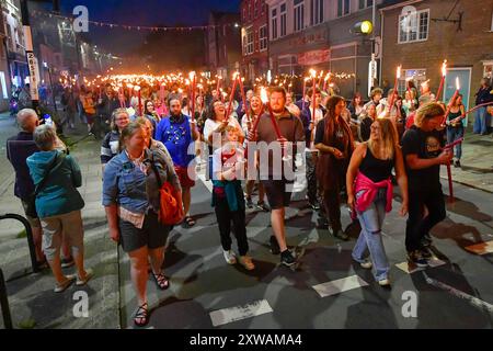 Bridport, Dorset, Royaume-Uni. 18 août 2024. Des centaines de personnes portant des torches flamboyantes participent à la procession annuelle des torches du carnaval de Bridport. La procession de Two Mile a commencé à l'hôtel de ville de Bridport et s'est terminée à East Beach à West Bay dans le Dorset. Crédit photo : Graham Hunt/Alamy Live News Banque D'Images