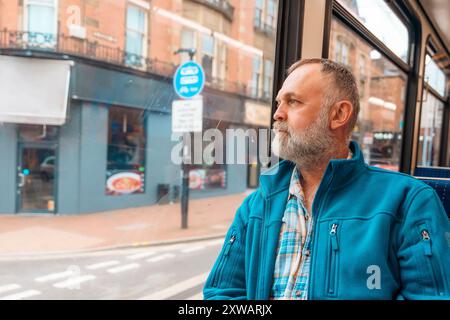 portrait d'un homme barbu dans une veste bleue parlant au téléphone dans un bus ou un tram. Concept de style de vie Banque D'Images