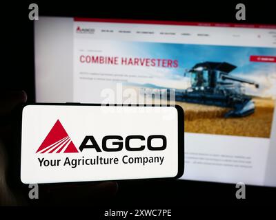Personne tenant le téléphone portable avec le logo de la société américaine de machines agricoles AGCO Corporation devant la page Web. Concentrez-vous sur l'affichage du téléphone. Banque D'Images