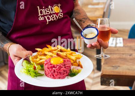 La Buvette, bar à Saint-Maximin (nord de la France). Serveur apportant un steak tartare avec des frites Banque D'Images