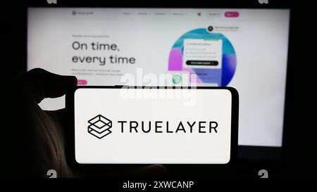 Personne tenant le téléphone portable avec le logo de la société britannique de paiements bancaires TrueLayer devant la page Web de l'entreprise. Concentrez-vous sur l'affichage du téléphone. Banque D'Images