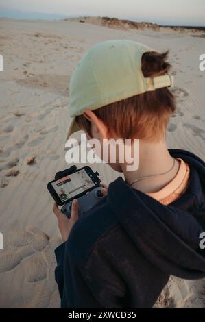 Adolescent garçon contrôle un drone tout en se tenant debout sur un terrain sablonneux Banque D'Images