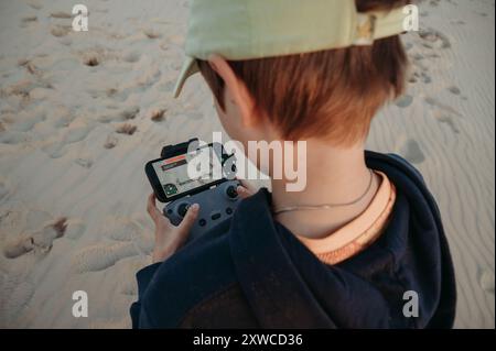 Adolescent garçon contrôle un drone tout en se tenant debout sur un terrain sablonneux Banque D'Images