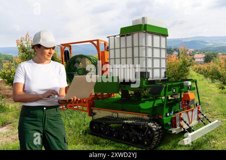 Farmer contrôle un pulvérisateur robot autonome dans un jardin fruitier. Concept d'agriculture intelligente.. Banque D'Images