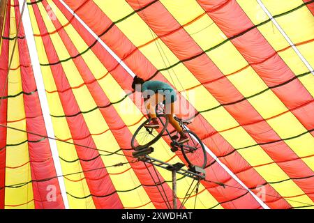 Sirajganj, Sirajganj, Bangladesh. 19 août 2024. Un membre de ''The New Lucky 7 Circus'' divertit le public en effectuant un numéro d'équilibre tout en se tenant debout sur un vélo à Sirajganj, au Bangladesh. Le cirque est une forme de divertissement populaire au Bangladesh qui est presque en train de disparaître. Une tradition de presque cent ans, ce jeu est montré dans une immense tente colorée. Ici, les artistes mettent en valeur leurs compétences à travers des cascades, acrobaties, clowns, marionnettes, marche serrée. (Crédit image : © Syed Mahabubul Kader/ZUMA Press Wire) USAGE ÉDITORIAL SEULEMENT! Non destiné à UN USAGE commercial ! Banque D'Images