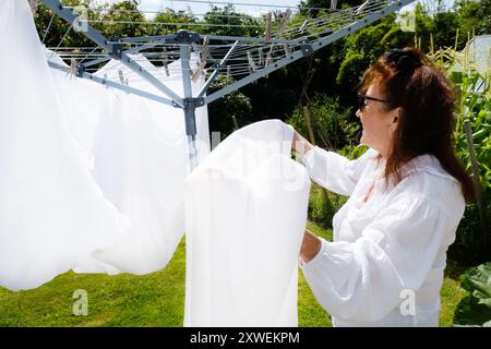 Femme mature traînant des draps de lit blancs sur une ligne de vêtements rotative - John Gollop Banque D'Images