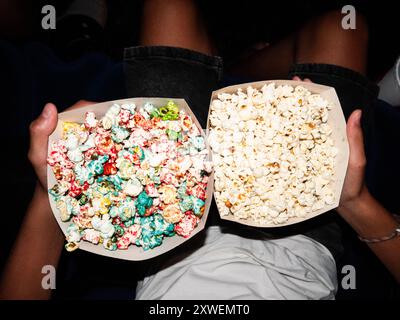 Garçon tenant deux récipients de pop-corn, l'un rempli de pop-corn sucré et coloré et l'autre de pop-corn ordinaire, classique, en attendant dans le ciné Banque D'Images