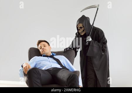 Grim Reaper debout par l'homme mort dans la chaise sur fond gris Banque D'Images