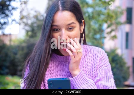Femme surfant sur Internet à l'aide d'un appareil mobile avec le visage surpris à l'extérieur. Banque D'Images