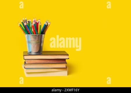 Un seau avec des crayons de couleur sur des livres sur un fond jaune avec espace de copie Banque D'Images