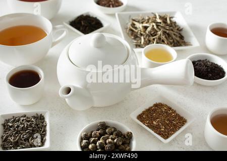 Une vue d'une théière blanche entourée d'une variété de thé en feuilles en vrac. Banque D'Images