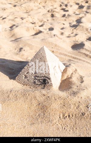 Une petite réplique en pierre d'une pyramide est cachée dans la plage de sable, créant un paysage pittoresque et symbolique Banque D'Images