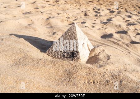 Une petite réplique en pierre d'une pyramide est cachée dans la plage de sable, créant un paysage pittoresque et symbolique Banque D'Images