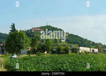 Rovato, Italie - 8 juin 2023 : une petite voiture roule le long d'une route rurale, en passant par un champ de maïs vert, avec une belle villa donnant sur le cou Banque D'Images