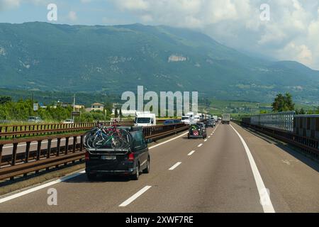 Ossenigo, Italie - 8 juin 2023 : les véhicules circulent le long d'une autoroute panoramique avec en toile de fond des montagnes majestueuses tandis que les vélos reposent sur une voiture sous le Banque D'Images