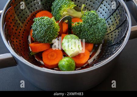 Panier vapeur pliable dans une casserole avec brocoli, carottes et choux de Bruxelles. La cuisson à la vapeur permet de conserver les nutriments essentiels, les saveurs et les Banque D'Images