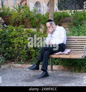 Jérusalem, Israël - 20 juin 2023 : un homme juif orthodoxe profondément dans la pensée ou somnolant, sur un banc dans une rue de Jérusalem, Israël. Banque D'Images