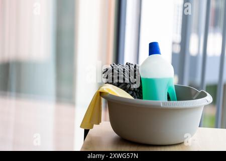 un seau de produits de nettoyage sur une table contre le verre de fenêtre propre brillant Banque D'Images