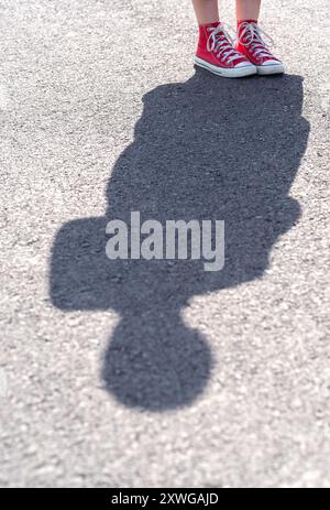 Baskets rouges et ombres. Silhouette d'une jeune fille sur une route asphaltée. Banque D'Images