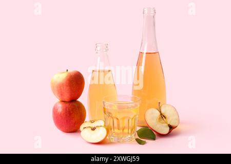 Composition avec bouteilles et verre de cidre de pomme frais sur fond rose Banque D'Images