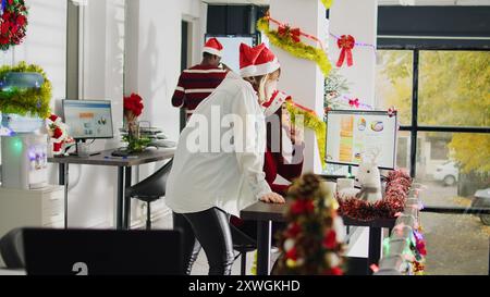 Employé asiatique travaillant pendant la période de Noël dans un bureau décoré festif, montrant les progrès de l'audit du chef d'équipe. Projet de résolution comptable dans le lieu de travail orné de Noël multiethnique pendant la saison des fêtes Banque D'Images