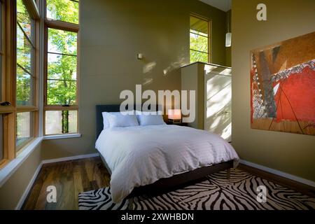 Chambre avec lit blanc et tapis à motif zèbre et grandes fenêtres montrant des arbres verts à l'extérieur Banque D'Images