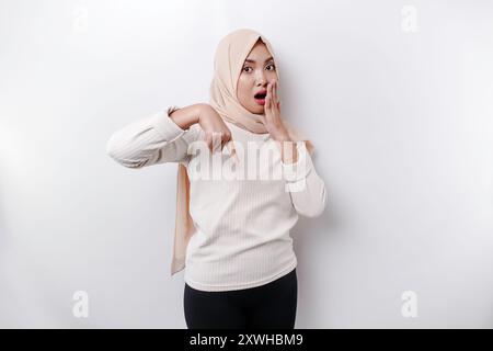 Femme musulmane asiatique choquée portant un foulard pointant vers l'espace de copie en dessous d'elle, isolée par fond blanc. Banque D'Images