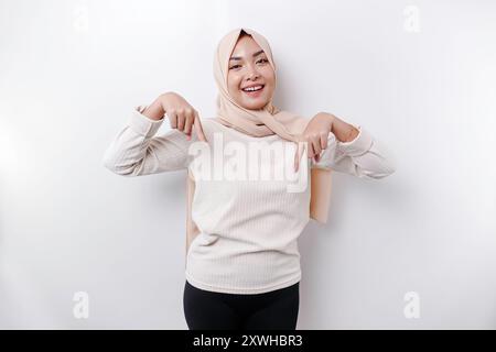 Femme musulmane asiatique excitée hijab pointant vers l'espace de copie en dessous d'elle, isolé par fond blanc. Banque D'Images