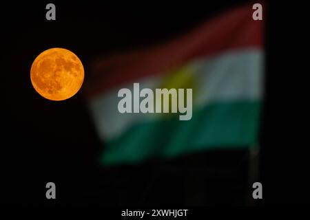 Duhok, Irak. 19 août 2024. La super lune se lève derrière le drapeau de la région du Kurdistan dans le ciel de la ville de Duhok, au nord de l'Irak. (Photo de Ismael Adnan/SOPA images/SIPA USA) crédit : SIPA USA/Alamy Live News Banque D'Images