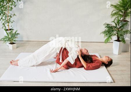 Masseuse faisant massage yoga thaïlandais. Thérapeute de femme faisant le traitement de massage traditionnel, étirant le corps de la patiente féminine. Client allongé sur tapis, profitant d'un massage des mains dans une atmosphère calme. Banque D'Images