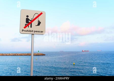 Un panneau de non-pêche proéminent est affiché près des eaux calmes de l'océan sous le ciel bleu. Encourager le respect et la prise en charge des plans d'eau naturels en imposant le no-fishi Banque D'Images