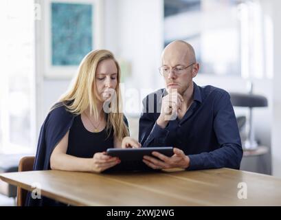 Symbolfoto. Eine Frau und ein Mann sitzen zusammen an einem Tisch mit einem Tablet und unterhalten sich. Berlin, 13.08.2024. Berlin Deutschland *** Sy Banque D'Images