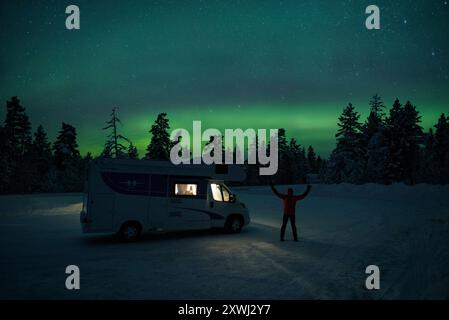 Aurores boréales au-dessus d'un camping-car et d'une forêt enneigée la nuit (Laponie, Finlande) ESP : Aurora boréale sobre una autocaravana y un bosque nevado, Laponie Banque D'Images