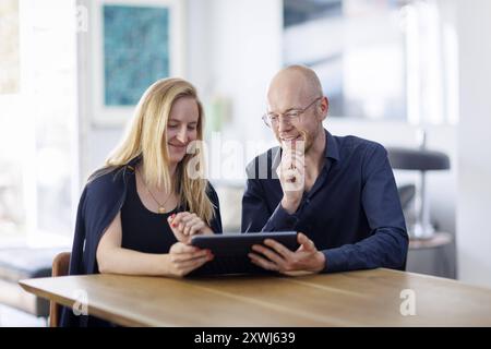 Symbolfoto. Eine Frau und ein Mann sitzen zusammen an einem Tisch mit einem Tablet und unterhalten sich. Berlin, 13.08.2024. Berlin Deutschland *** Sy Banque D'Images