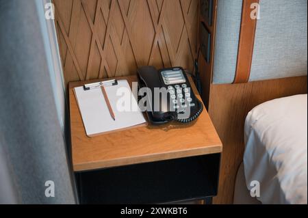 Téléphone de service avec carnet de papier, crayon sur la table de chevet dans la chambre Banque D'Images