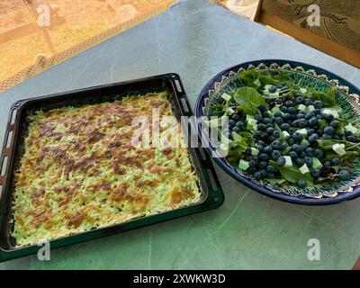 Salade estivale avec légumes verts, fromage, moutarde française et bleuets. À côté, il y a une plaque de cuisson avec des pommes de terre rôties. Banque D'Images