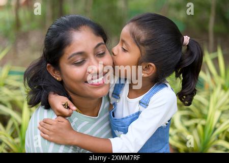 Adorable petite fille partage un baiser d'amour avec sa mère dans un écrin de verdure. Banque D'Images