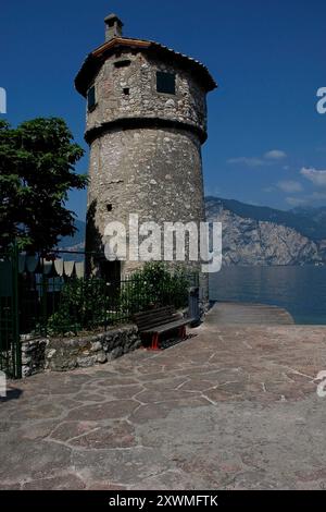 Tour circulaire en pierre surplombant le lac de Garde à Cassone di Malcesine, un village de Vénétie, en Italie, sur la rive est du lac de Garde. Cette ancienne tour est connue sous le nom de la 'Toresela'. Une cheminée traditionnelle à persiennes s'élève au-dessus du toit de la tour en tuiles de terre cuite. Banque D'Images