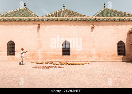 Une personne marchant dans une cour à l'architecture traditionnelle, avec un mur avec des fenêtres cintrées et un toit de tuiles. Le sol est aménagé avec vari Banque D'Images