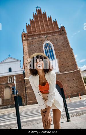 Femme élégante en haut orange et veste blanche pose devant une église européenne historique. Banque D'Images