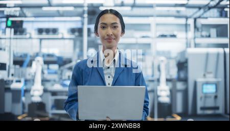 Portrait d'un bel ingénieur de fabrication électronique souriant, regardant la caméra. Jeune femme asiatique utilisant un ordinateur portable pour la recherche en ligne, la surveillance des systèmes industriels d'intelligence artificielle Banque D'Images