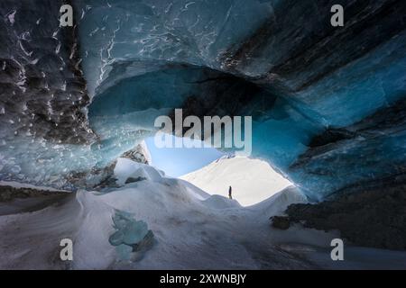 Vue du paysage hivernal d'un randonneur debout sur un rocher enneigé, explorant une grotte de glace à Langgletscher Loetschental Suisse Banque D'Images