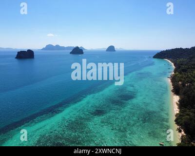 Vue aérienne de la plage de Ko Ngai avec son incroyable récif corallien et ses eaux turquoise et d'autres îles Trang en arrière-plan Banque D'Images