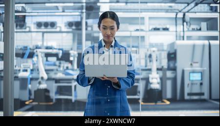 Portrait d'un bel ingénieur de fabrication électronique souriant et travaillant. Jeune femme asiatique utilisant un ordinateur portable pour la recherche en ligne, la surveillance des systèmes industriels d'intelligence artificielle Banque D'Images